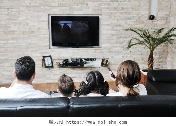 一家四口坐在沙发上看电视快乐年轻的家庭有乐趣和手提电脑在家里工作